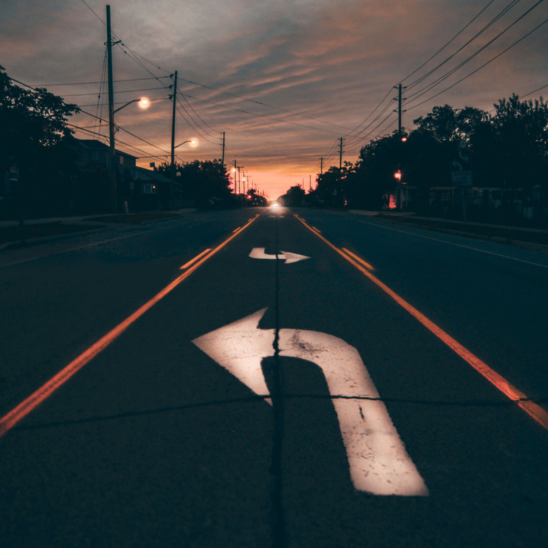 Eine dunkle Straße mit Abbiegepfeil zum Sonnenuntergang